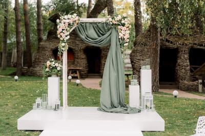 Exquisite Outdoor Wedding Setup with Wedding Arch, Drapes, Flowers, Candle Shades and Lanterns