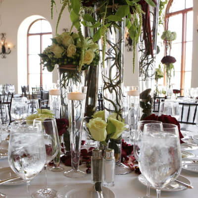 Fanciful Party Table Decor With Tablecloth, Trumpet Vase, Flowers, Petals, Greenery Spray, & Candles
