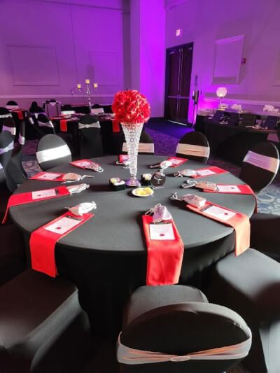 Sophisticated Black & Red Table Setting with Crystal Accents, White Chair Sashes, and Floral Vase
