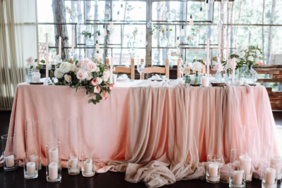 Soft Pastel Table Setting with Draped Tablecloths, Delicate Flowers, and Tall Candle Accents