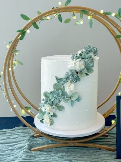 Corrected: Minimalist Cake Display with Gold Circle Stand, Glowing Fairy Lights, and Leaf Accents