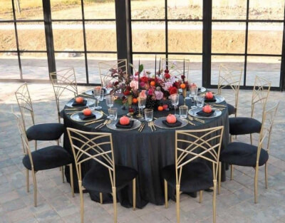 Chic Black and Gold Tablescape with Jewel-Toned Florals, Clear Plates, Glassware, and Luxe Seating