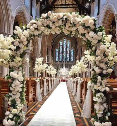 Romantic Wedding Ceremony Featuring White Rose Arch, Draped Pew Accents, and Aisle Décor