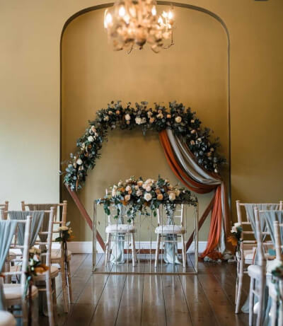 Elegant Indoor Ceremony Setup with Floral Arch, Draped Accents & Chair Décor