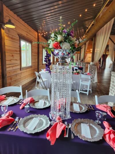 Stunning Barn-Style Setup Featuring Crystal Centerpieces, Purple Linens, Coral Napkins & Silver Dinn